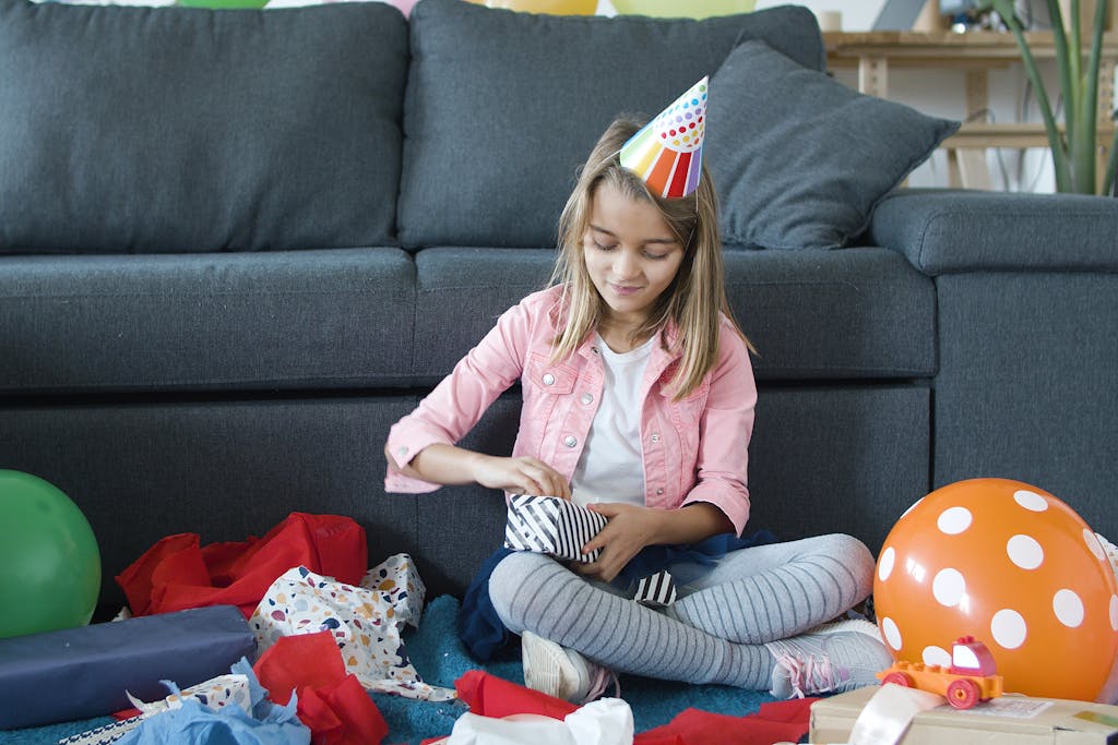 A girl in a party hat opens gifts in a vibrant and joyful indoor birthday setting.